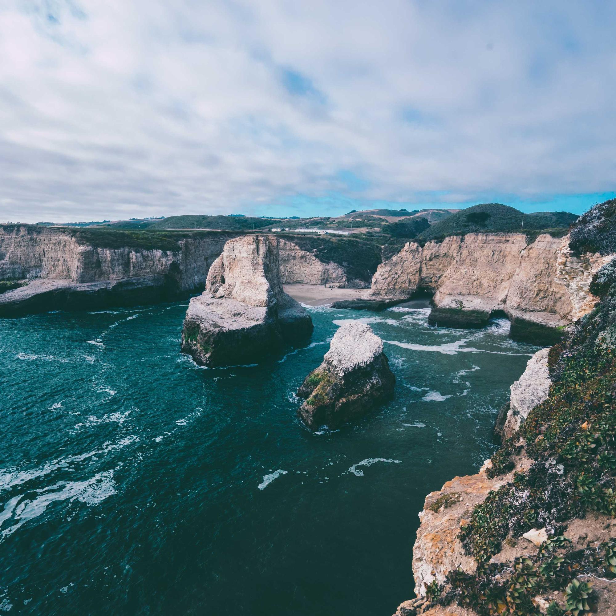 Coastă stâncoasă cu faleze albe și apă de un verde-turcoaz, sub un cer cu nori